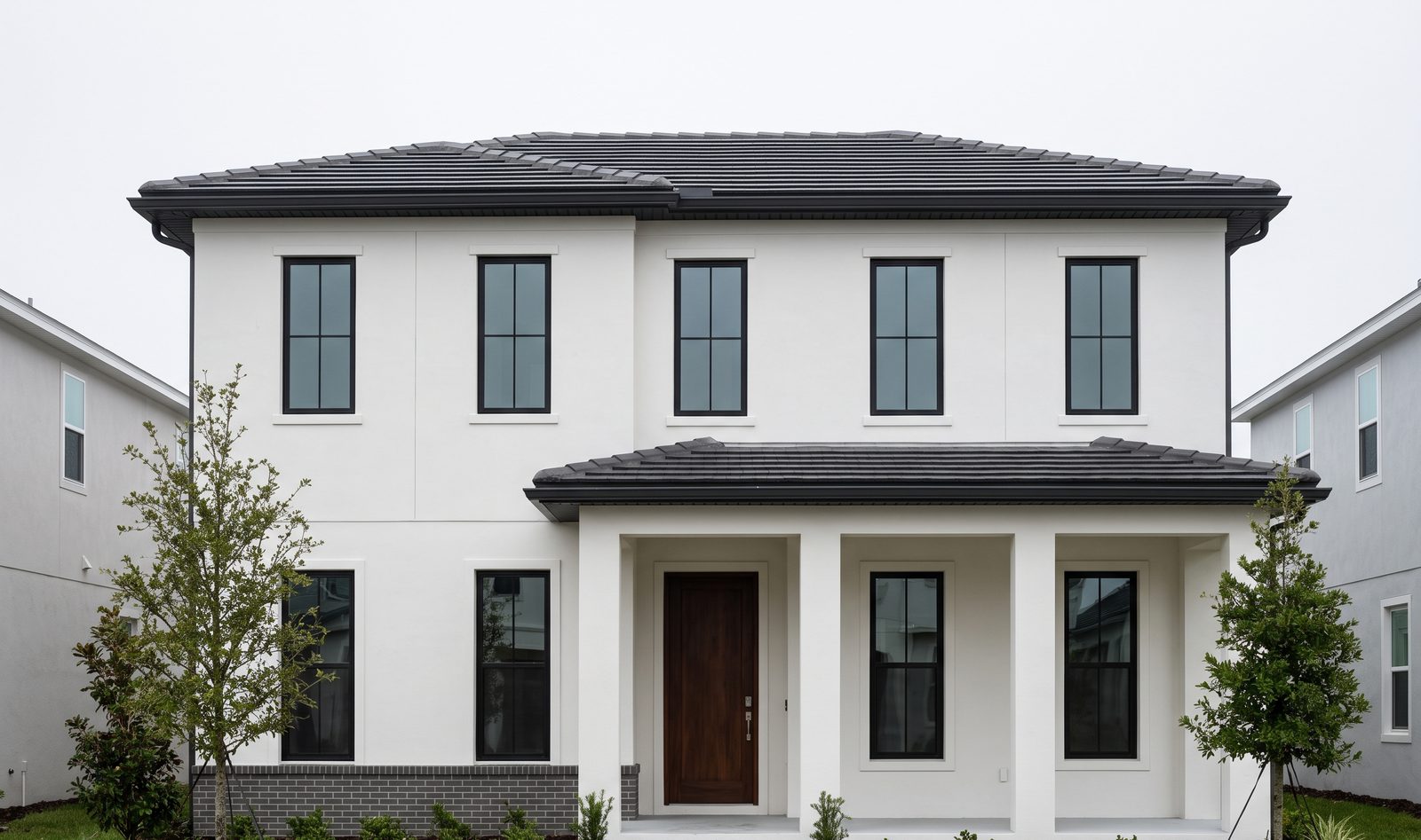 The Laureate Park house shot dead centred under flat overcast, white stucco walls, black windows and a tile hip roof