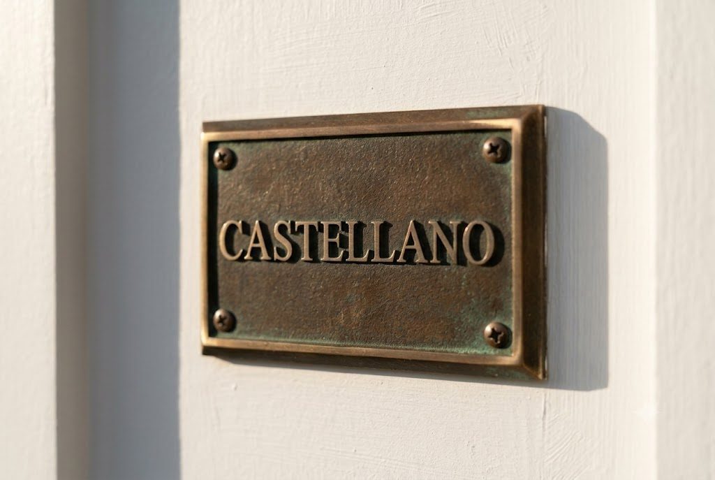 A cast bronze plate reading Castellano, green with age, screwed to the white painted trim beside a front door