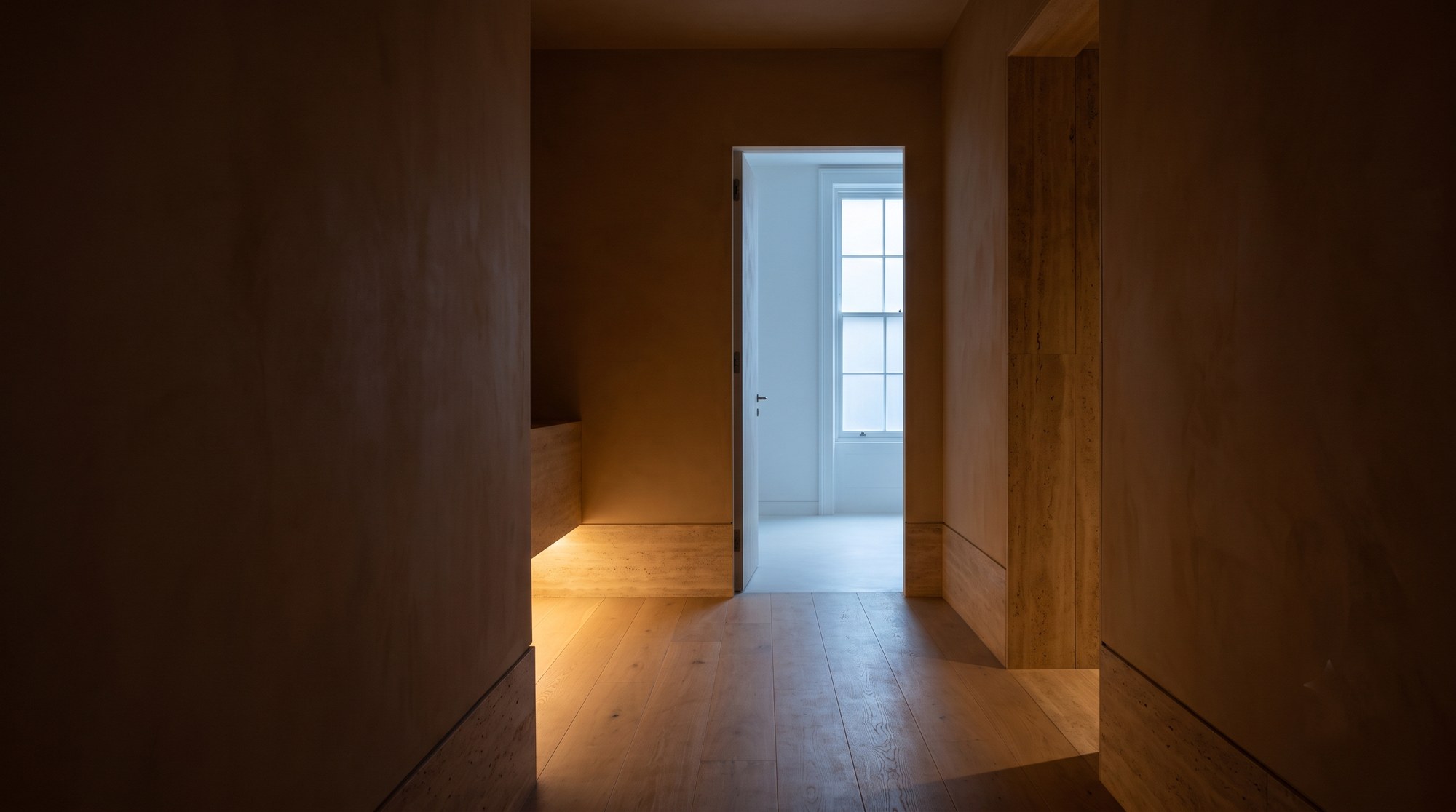 A dim oak and plaster corridor at Northlight, with cool daylight falling from a tall window in the room at the far end.