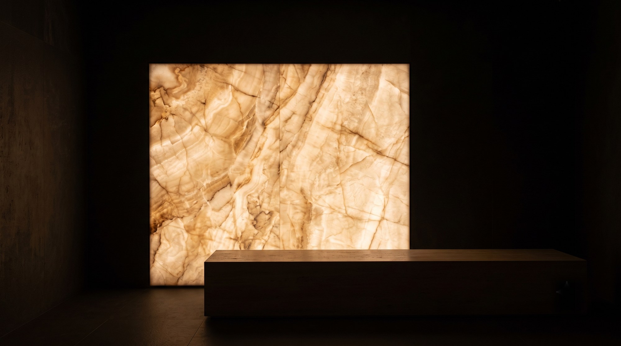 A backlit slab of alabaster lit warm from behind a low oak bench in an otherwise dark room.
